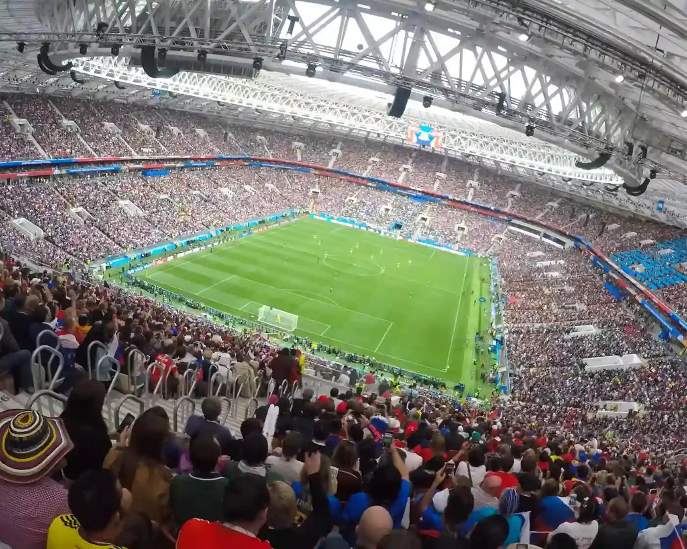 Wide view of a packed football stadium with a green pitch and crowds in the stands—scale of sports fandom and live events
