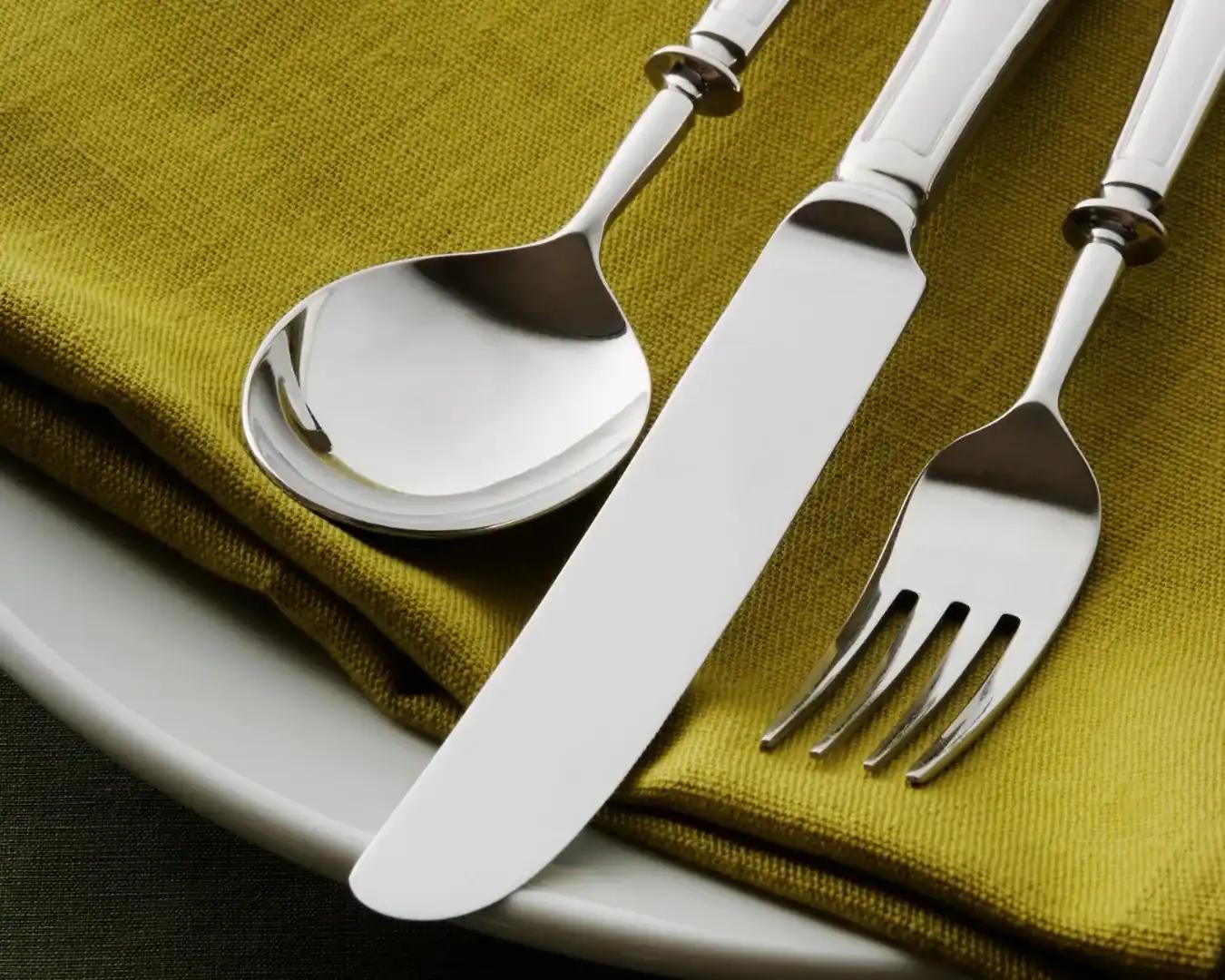 Close-up of elegant silver cutlery on an olive green napkin and white plate, representing the hospitality and restaurant sector.