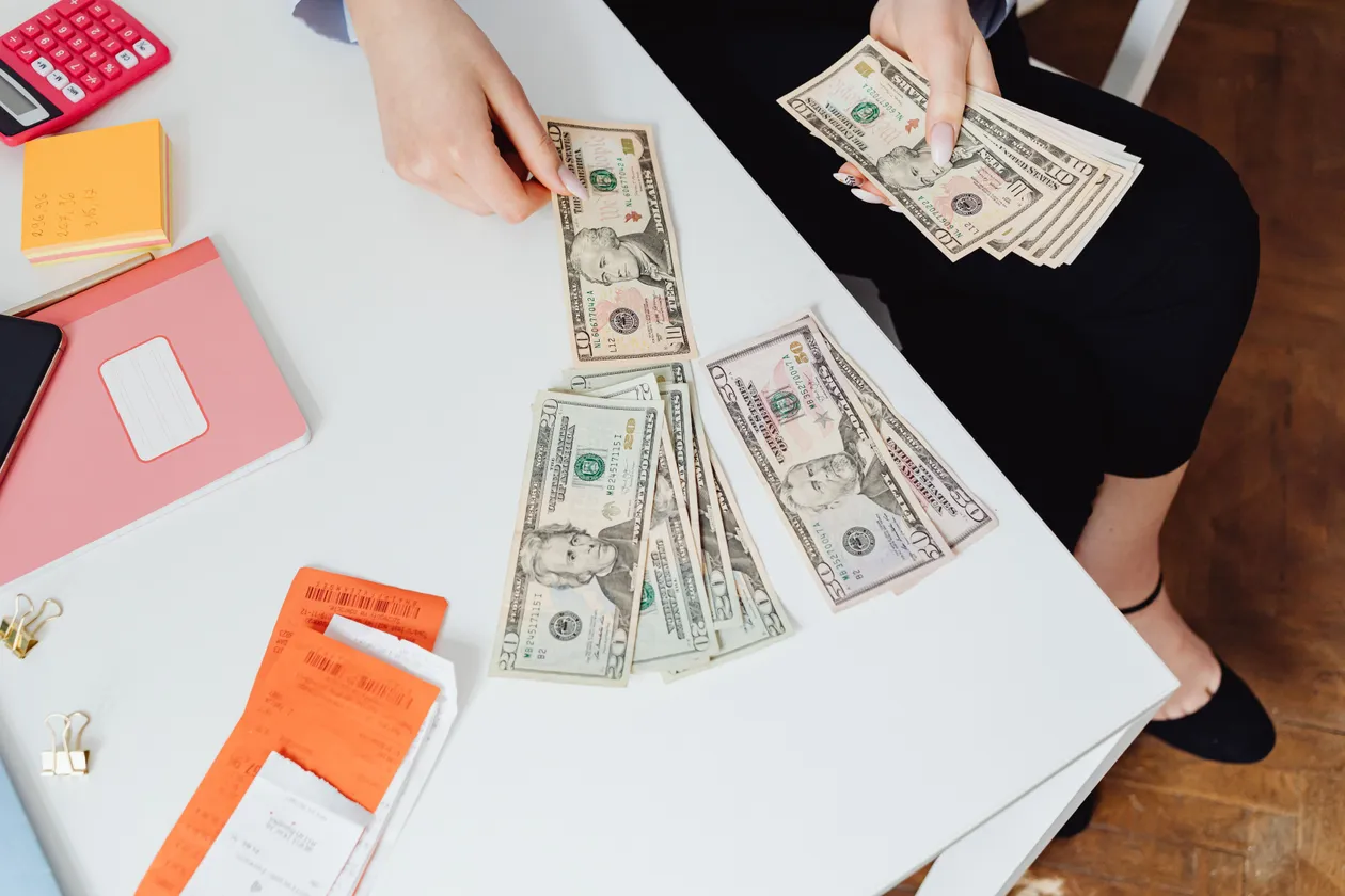High-angle shot of a person counting US dollar bills at a white desk