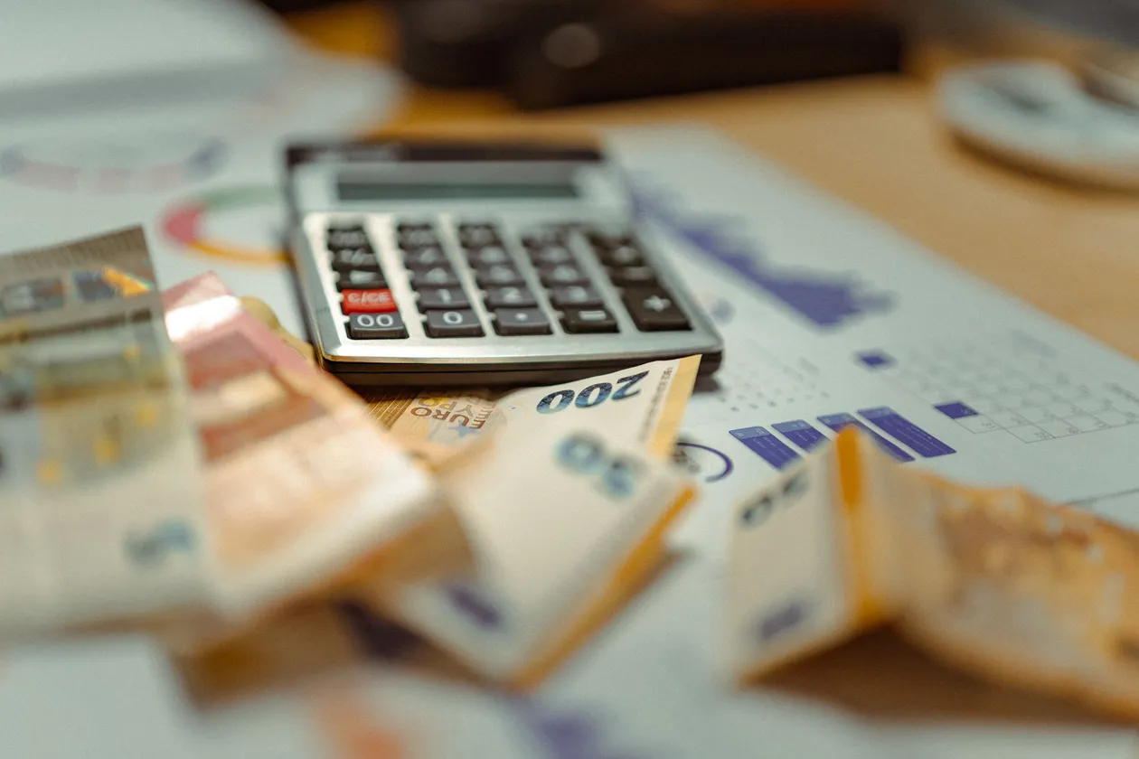 Close-up of a calculator resting on scattered banknotes and printed financial charts arranged on a desk
