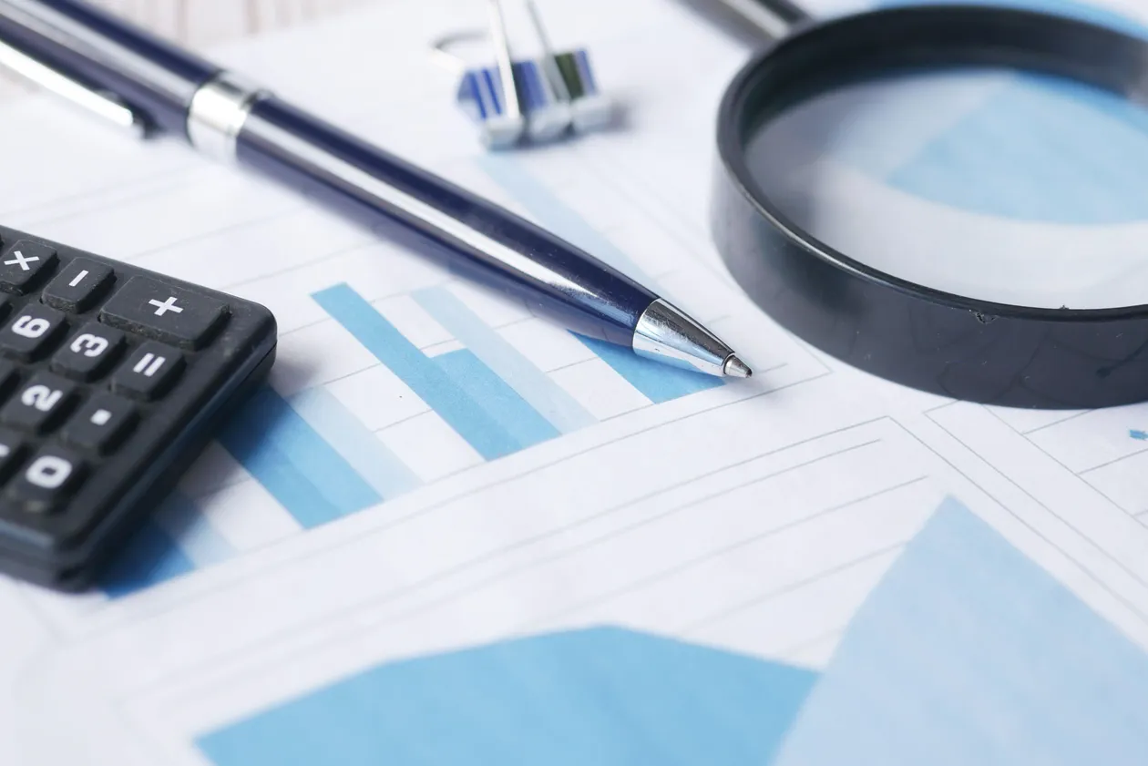 Pen, calculator, and magnifying glass resting on printed bar-chart documents