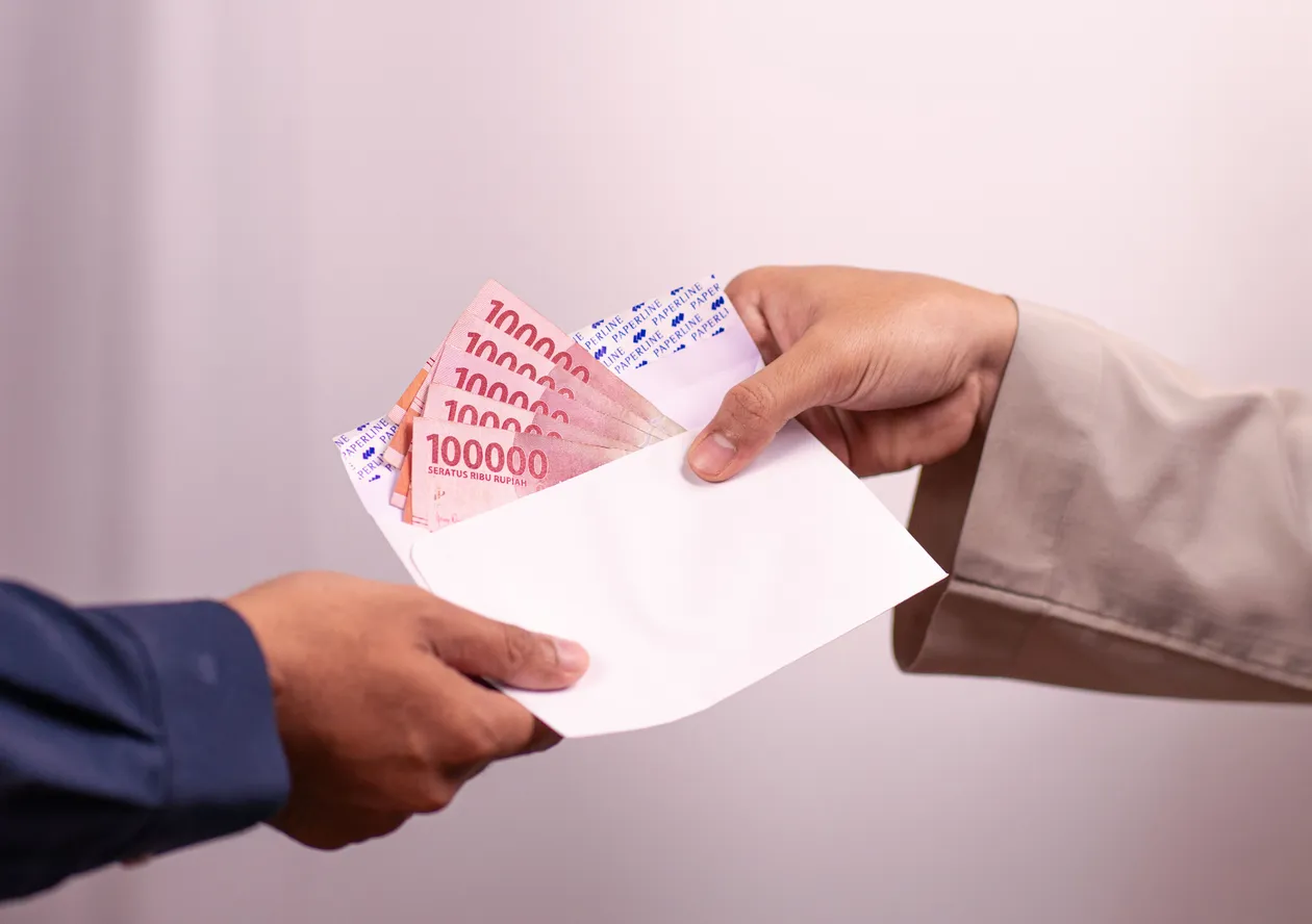 Hands giving and receiving Indonesian rupiah inside an envelope