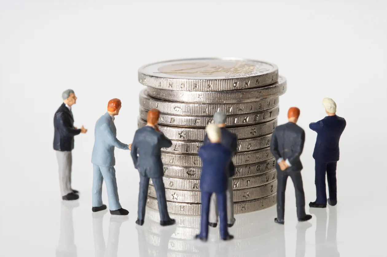 Miniature human figures standing beside stacked silver coins symbolizing workforce and capital