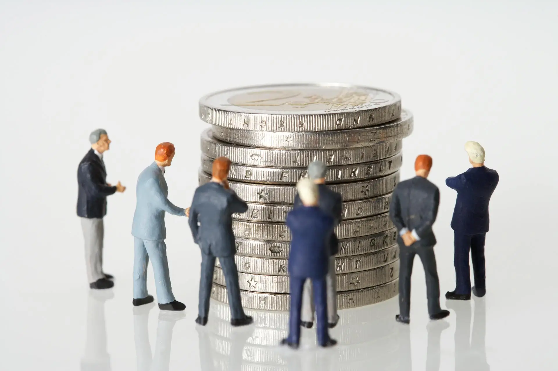 Human figurines standing beside silver coins, illustrating business strategy and financial asset management.