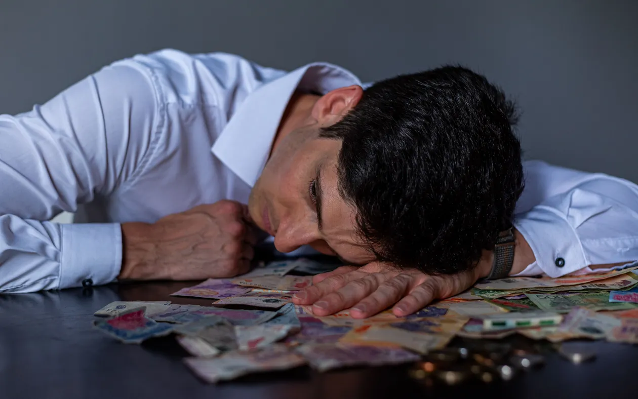 A stressed man sitting at a table with Argentine peso bills